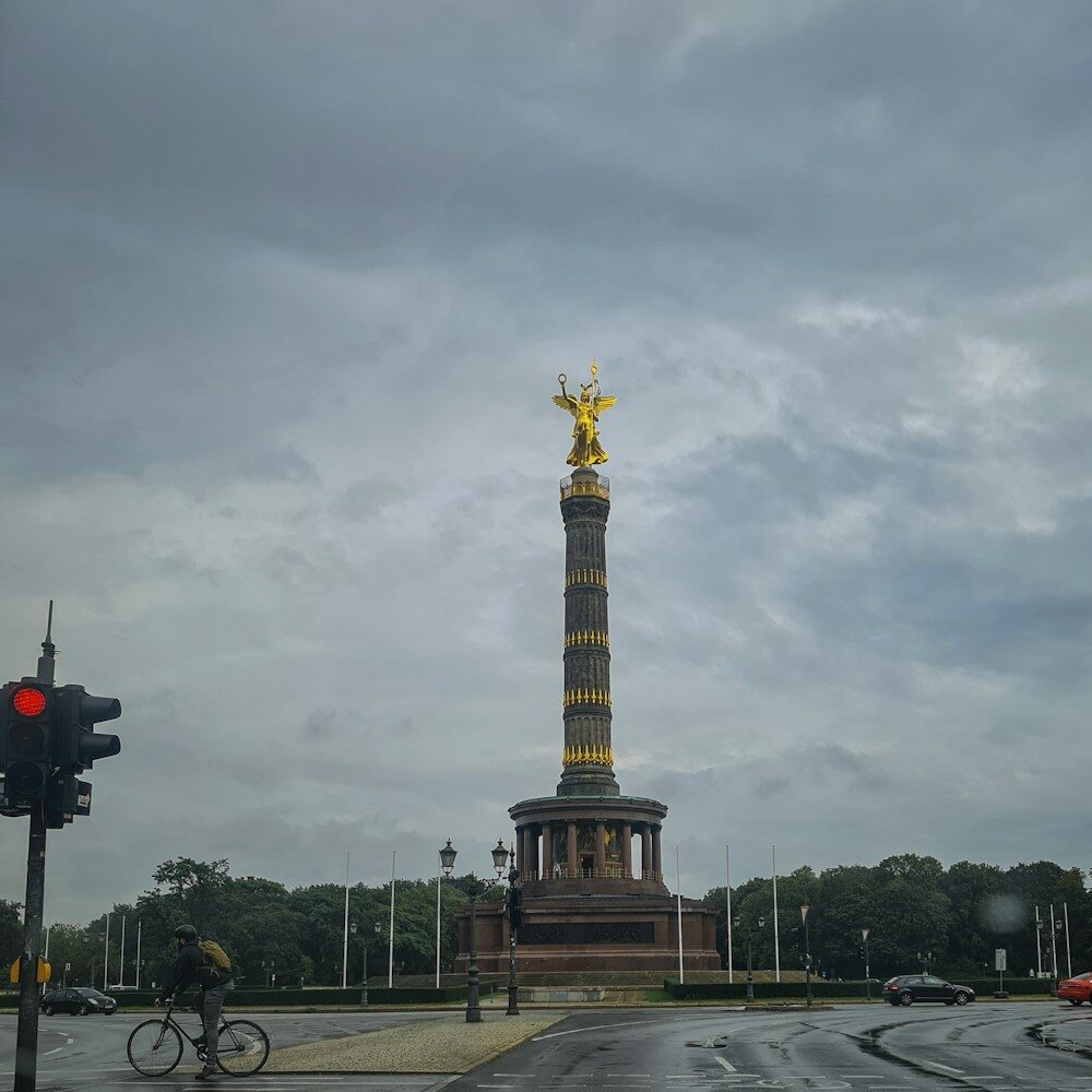 a tall tower with a gold top with Berlin Victory Column in the background