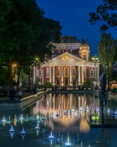 brown mansion house near rectangular swimming pool surrounded with tall and green trees during night time